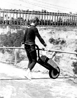 Man riding a bicycle on tightrope across a river